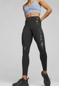 Leggings neri con pannelli laterali lucidi, vita alta e design aderente, abbinati a un reggiseno sportivo azzurro chiaro. Tessuto testurizzato in tutto.