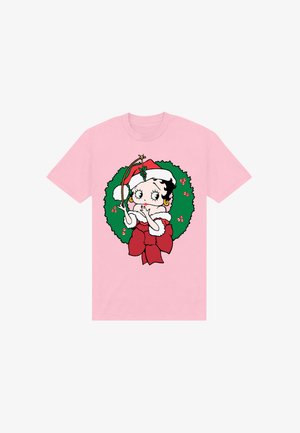 T-shirt rosa con un personaggio dei cartoni animati dai capelli neri e ricci, un cappello di Babbo Natale rosso, circondato da una ghirlanda verde con accenti rossi.