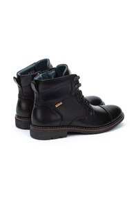 Botas de tobillo de cuero negro con paneles texturizados, con cordones en la parte delantera, puntera redonda y suela marrón en contraste. Presenta un logotipo cerca del tobillo.