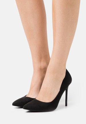 Černé semišové vysoké podpatky s designem špičaté špičky. Mají štíhlý stiletto podpatek a hladký povrch, což zdůrazňuje minimalistickou eleganci.