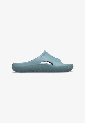 Lichtblauwe schuifslipper van flexibel rubber. Heeft een gladde oppervlakte, open teen en uitsparingen aan de zijkant. Textuur op de zool voor grip.