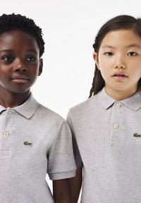 Polo shirt grigi con tessuto testurizzato, con colletto e tre bottoni. Ciascuno presenta un piccolo logo di coccodrillo verde sul petto.