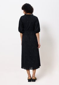 Schwarzes Maxikleid mit strukturiertem Blumenmustern, puffigen Ärmeln und tailliertem Bund, in Midi-Länge mit transparenter Saumlinie.