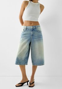 Höga jeans culottbyxor i ljusblått med en urtvättad look, med fem fickor och knäppning. Bärs med en figurnära vit crop top och svarta sandaler.