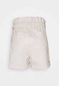 Shorts en similicuir crème avec une ceinture extensible, des revers roulés et deux poches arrière ornées d'un détail de couture subtil.