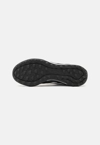 Suola di scarpa sportiva nera con gomma testurizzata, dotata di borchie arrotondate e un design curvo prominente, che evidenzia la presa e la durata.