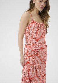 Robe rouge avec des motifs de feuilles blanches ; sans manches avec des bretelles fines ; design avec taille froncée ; texture de tissu lisse.