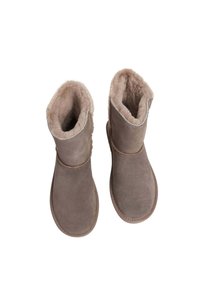 Botas de tobillo de ante marrón con un suave forro de piel de pelo, punta redondeada y diseño con puños. Detalles cosidos visibles alrededor de los bordes.
