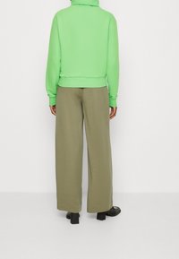 Zelená mikina s vysokým límcem a žebrovaným lemem, doplněná olivovými kalhotami s širokými nohavicemi. Oblečení má uvolněný střih a hladkou texturu.