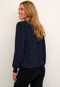 Navy blue blouse with textured fabric, long puffed sleeves, and elastic cuffs. Features a rounded neckline and a relaxed fit.