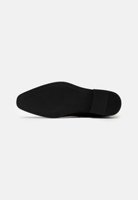 Černá podrážka obuvi s hladkým designem, zaoblenou špičkou a texturovaným protiskluzovým vzorem. Minimalistické akcenty, gumový materiál a plochý podpatek.