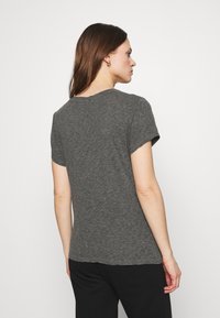 Pelēks īsām piedurknēm T-krekls, kas izgatavots no mīksta, teksturēta auduma. Tam ir noapaļots kakla izgriezums un brīvs piegriezums, demonstrējot vienkāršu, ikdienišķu dizainu.