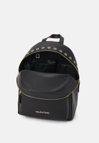 Svart läderryggsäck med guldhardware, cirkulära öglor, dragkedjestängning upptill och en framficka med en slät yta.