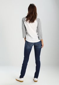 Vit och grå baseballtröja med 3/4 ärmar, kombinerad med mörkblå smala jeans och vita sneakers, sedd bakifrån.