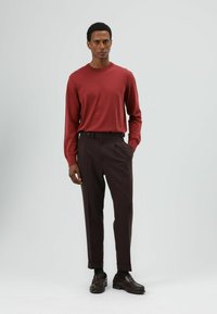 Rood shirt met lange mouwen en ronde hals, gecombineerd met donkerbruine, getailleerde broek met smalle pasvorm en boorden. Bruine loafers maken de outfit compleet.