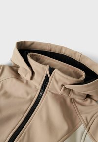 Beige Zip-up-Hoodie mit weicher Textur, schwarzen Akzenten, gefütterter Kapuze und strukturierten Nähten für eine figurbetonte Passform.