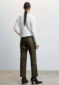 Weißer Pullover, olivgrüne Lederhose und schwarze Stiefeletten mit Absatz. Der Pullover hat ein schlichtes Design; die Hose ist mit Gesäßtaschen versehen.