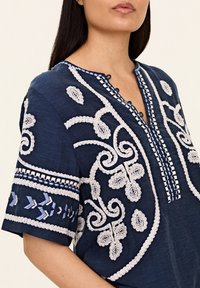 Marinblå tunika med vit broderi som har blomsterdesign, dekorativ sömnad längs halsringningen och broderade ärmar.