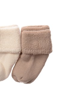 Zwei Paar Socken: ein cremefarbenes Paar mit einem strukturierten Bündchen und ein hellbraunes Paar mit einem gerippten Bündchen. Beide sind weich und elastisch.