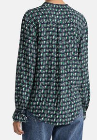 Blusa a maniche lunghe in tessuto blu navy con un motivo geometrico circolare in verde e rosa. Presenta una chiusura con bottoni sul retro e polsini arricciati.