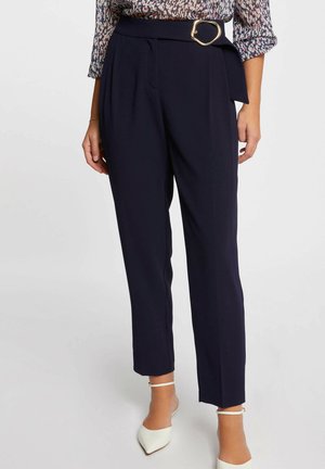 Pantaloni a vita alta blu navy con pieghe, dotati di una fibbia circolare dorata. Tessuto liscio, gambe affusolate e tasche laterali.