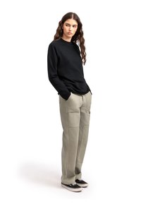 Maglietta nera a maniche lunghe, pantaloni cargo beige chiaro con tasche, tessuto strutturato, vestibilità comoda, abbinati a sneaker nere.
