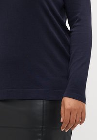 Langärmliges navyblaues Oberteil mit strukturiertem Strickfinish, kombiniert mit einem schwarzen Lederrock, der Saum und Handdetails zeigt.