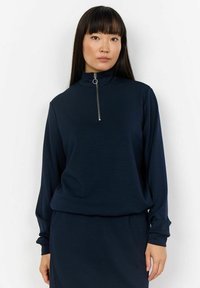Navy zip-up top with a high collar, made of soft fabric, featuring long sleeves and a relaxed fit, complemented by a small silver zipper detail.
