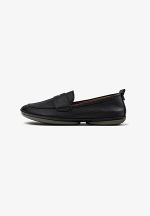 Mocasines de cuero negro con acabado texturizado, diseño sin cordones y suela plana de goma oliva. Presenta un pequeño detalle de correa en la parte delantera.