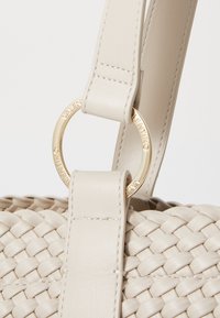 Sac à main en cuir tissé beige avec une texture lisse, doté d'un anneau en métal doré et d'une sangle robuste. Détails de couture visibles.