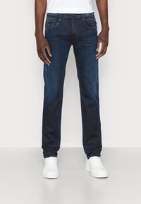 Dark blue denim jeans with a straight leg fit, five-pocket design, and subtle fading. Paired with white sneakers.