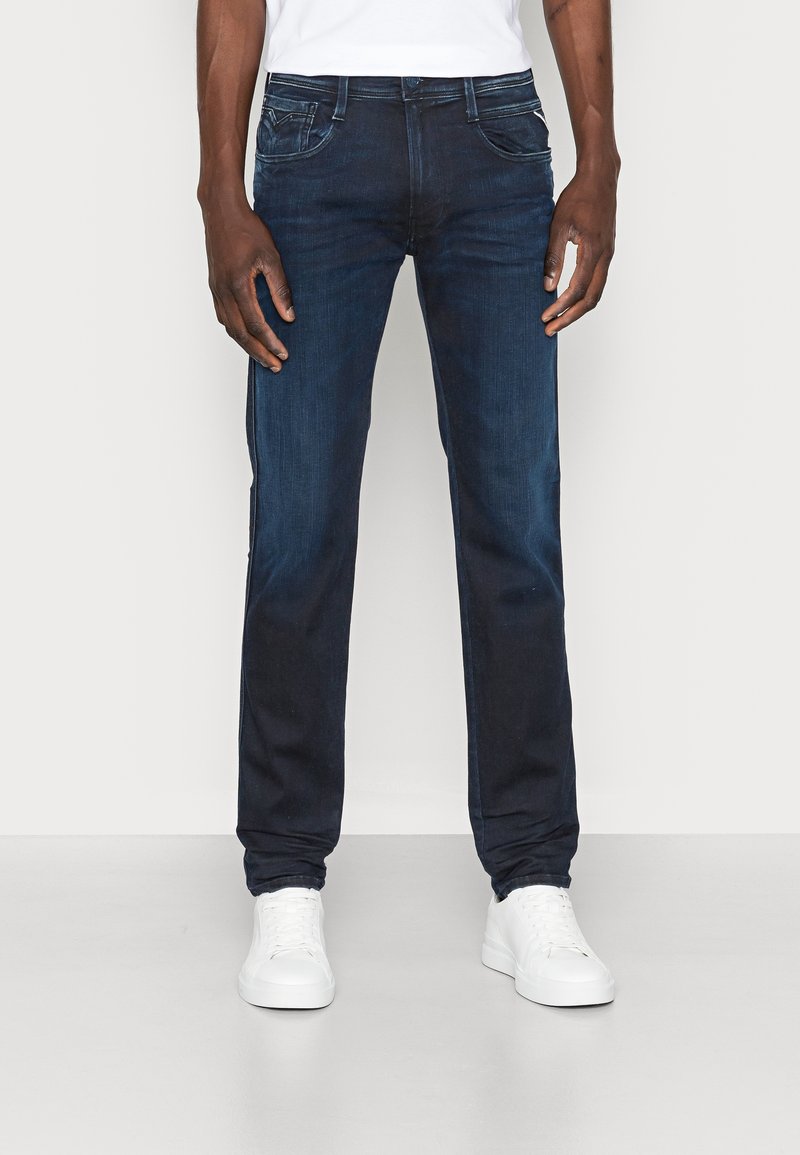 Dark blue denim jeans with a straight leg fit, five-pocket design, and subtle fading. Paired with white sneakers.