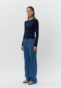 Laikku pitkähihaine paita yhdistettynä korkeavyötäröisiin sinisiin leveisiin farkkuihin ja beigeihin lenkkareihin. Silkkinen kangas, rento istuvuus ja suuret taskut.