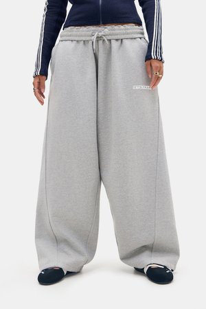 Persona que lleva pantalones deportivos holgados de color gris claro con cordón y texto en el muslo izquierdo, zapatos azul marino y camiseta de manga larga azul marino con rayas blancas.