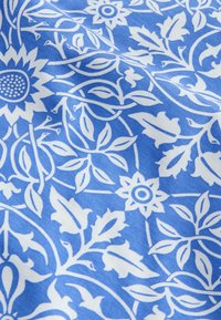 Baumwollstoff mit blauem Hintergrund, der ein weißes florales und Blattmuster zeigt, einschließlich Sonnenblumen und filigranen Rankenmustern.