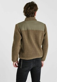 Fleecejack in olijfgroen met een gestructureerd, plush lichaam en een glad schouderpaneel. Beschikt over lange mouwen en een hoge kraag.