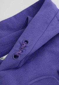 Fioletowa tkanina o gładkiej fakturze, z plecionym sznurkiem przez oczko oraz złożonym kołnierzem z warstwowym detalem projektowym.