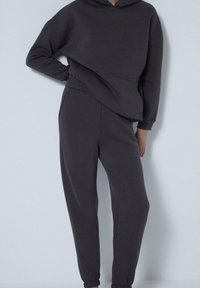 Donkergrijze, oversized hoodie met een buidelzak en joggers met elastische taille, gemaakt van zachte stof. Geleefde mouwen voor een getailleerde look.