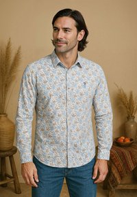 Lichtblauwe blouse met lange mouwen en een bloemenprint in bruin en crème. Heeft een knoopsluiting en een klein logo op de borst.