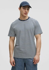 T-shirt rayé bleu marine et blanc avec un col rond, des manches courtes et une coupe décontractée, associé à un short bleu. Matière en coton doux.