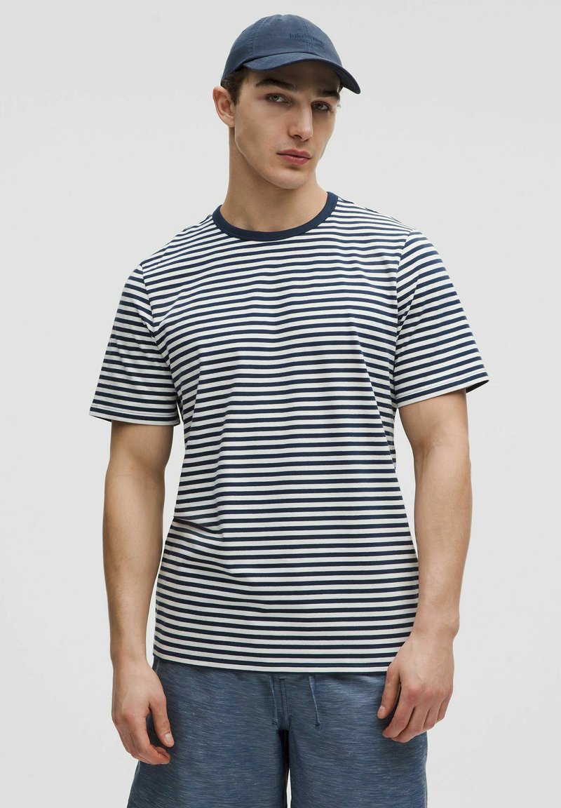 T-shirt rayé bleu marine et blanc avec un col rond, des manches courtes et une coupe décontractée, associé à un short bleu. Matière en coton doux.