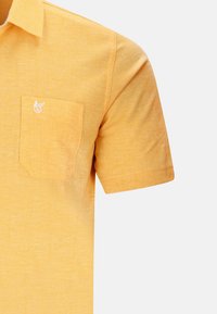 Chemise à manches courtes en tissu jaune vif, avec une poche sur la poitrine gauche ornée d'une broderie de logo blanc et d'une finition texturée.