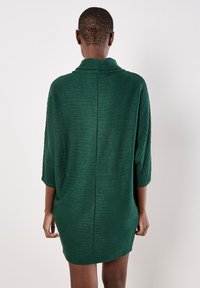 Abito lavorato a maglia verde con maniche a 3/4, tessuto testurizzato, vestibilità ampia e colletto alto. Presenta una cucitura centrale sul retro.