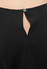 Peça de roupa preta com abertura em forma de gota nas costas, fechada por um botão redondo. Apresenta uma textura suave e detalhes de design simples.