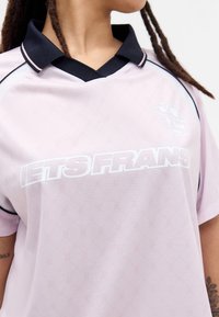 Ανοιχτό ροζ αθλητική μπλούζα με μαύρο γιακά και ήπιο υφασμάτινο σχέδιο. Διαθέτει έντονο λευκό κείμενο "LETS FRANS" στο μπροστινό μέρος.