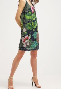 Mönstrad ärmlös klänning i mörka nyanser med gröna blad, rosa och vita blommor, samt en lös passform. Kompletteras med remsandaler.