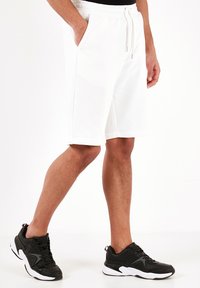 Hvide bomuldsblandede shorts med elastisk talje og snor. Har sidelommer og en afslappet pasform. Sættes sammen med sorte atletiske sneakers.