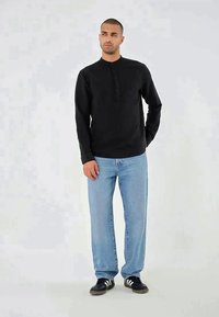 Camisa preta de manga longa com uma pala de botões, combinada com jeans de perna reta de um azul claro e ténis pretos.