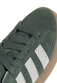 Zelená semišová teniska s bílými koženými pruhy, texturovanými detaily a plochými tkaničkami. Podešev z přírodní gumy.