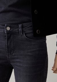 Tummansiniset farkut kapealla leikkauksella, joissa on klassinen viiden taskun malli, metalliset yksityiskohdat ja minimalistiset ompelut.